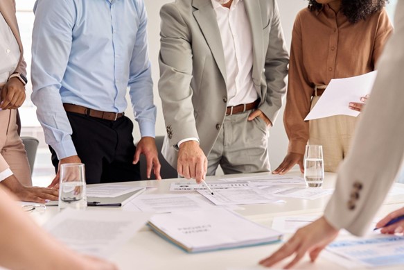 there is a white conference table that is has notebooks and papers on it with about four people looking down at the table.