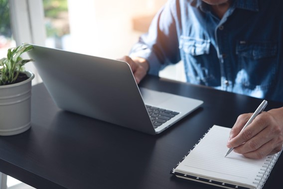 man on laptop. he is writing something in a notepad