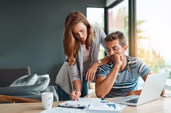 woman standing over a man who is sitting down. they are both looking down at papers.