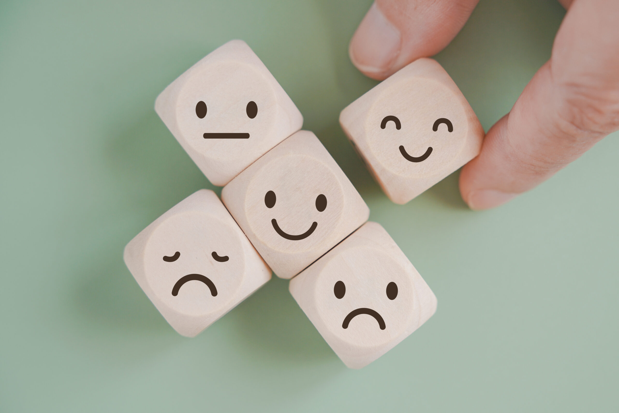 hand selected happy face wood cube and others on green background for customer service evaluation, feedback, satisfaction survey or mental heath concept