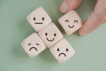 hand selected happy face wood cube and others on green background for customer service evaluation, feedback, satisfaction survey or mental heath concept