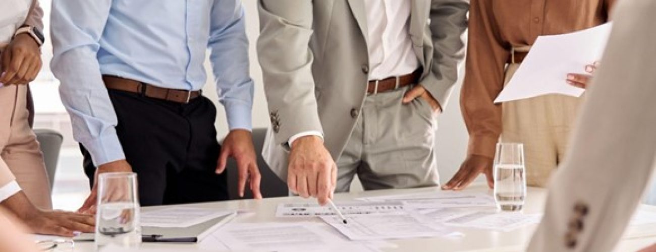 there is a white conference table that is has notebooks and papers on it with about four people looking down at the table.