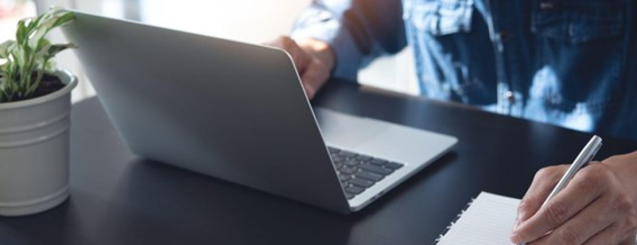 man on laptop. he is writing something in a notepad