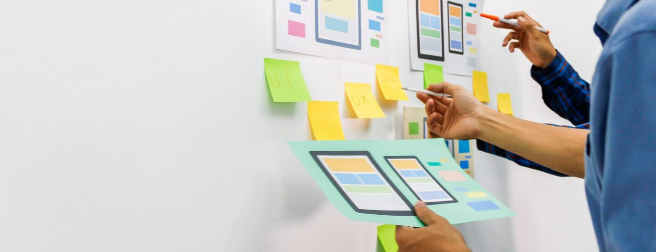 two people are standing infront of a white board but you only see their hands and arms. on the white board are post its