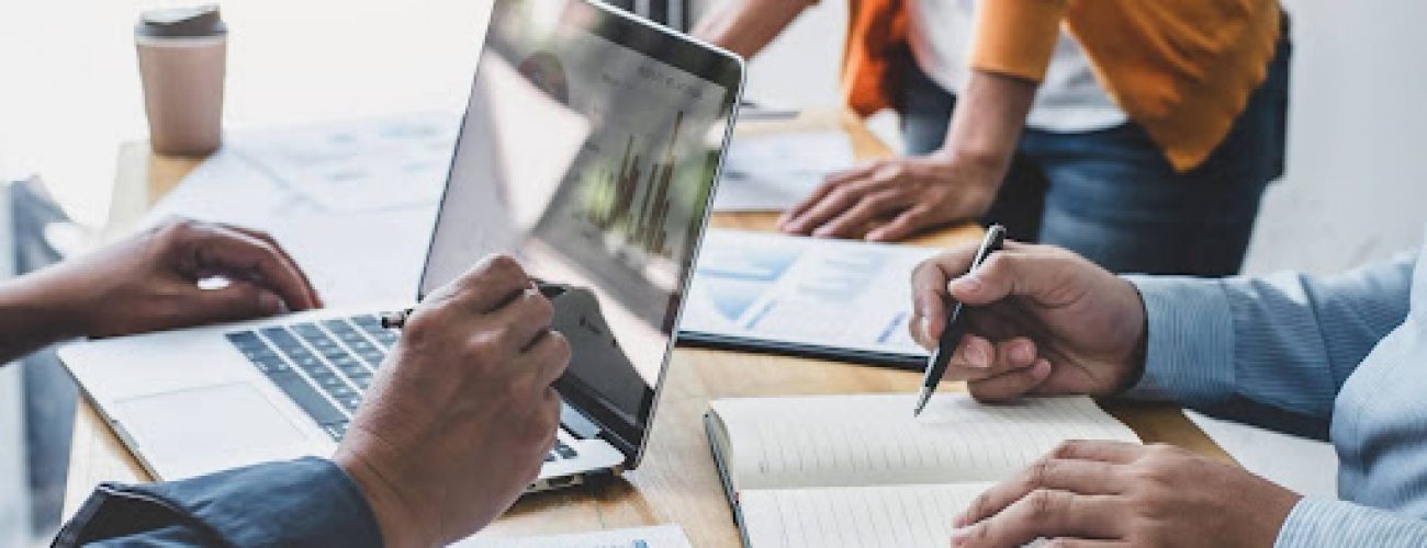unnamed (1) Business professionals collaborating at a table, focused on their laptops and engaged in discussion.